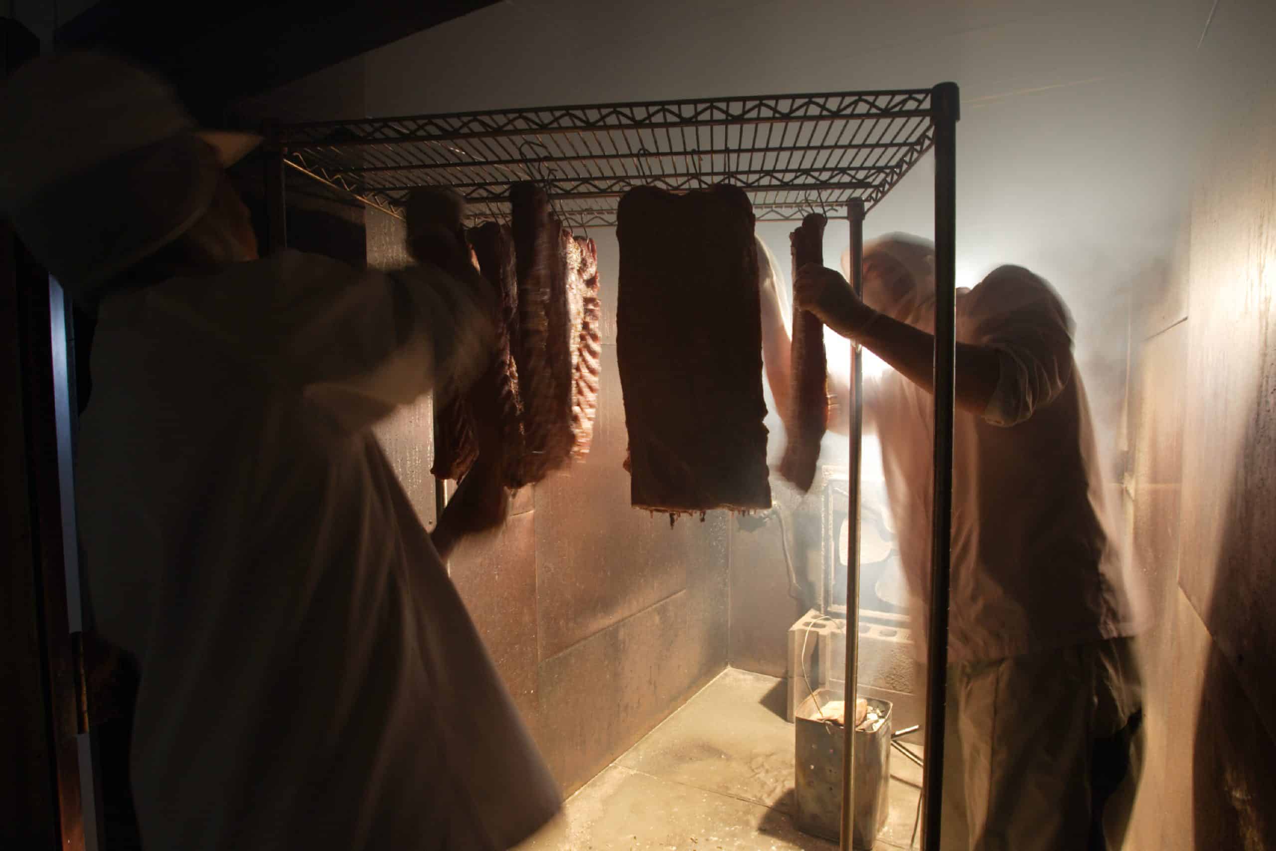 燻煙庫の中で肉の状態を見ながら作業するスモークマン